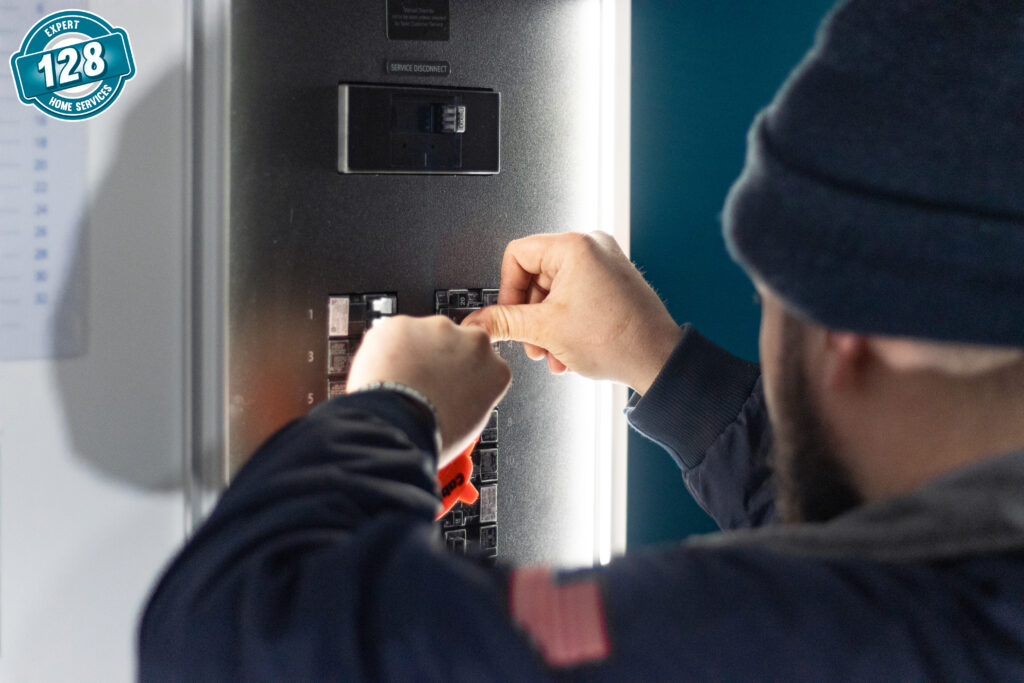 A technician adjusting switches in an electrical panel, focusing intently on the task, wearing a blue jacket and a beanie.