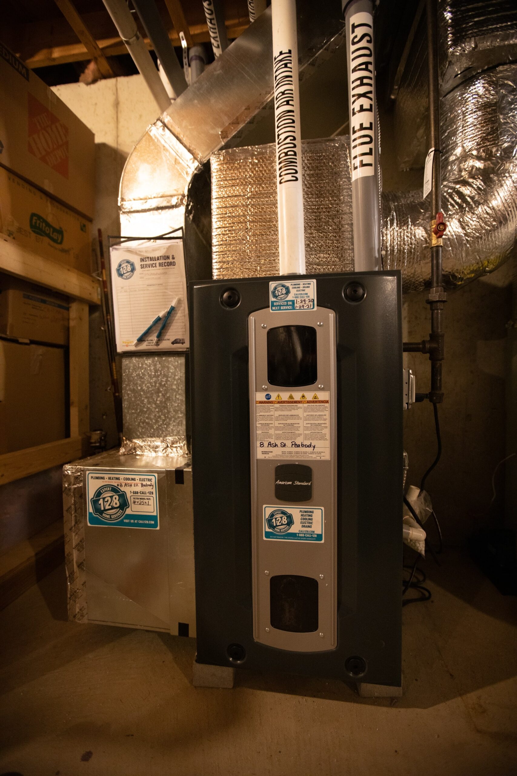 A modern HVAC system installed in a basement, featuring pipes labeled "fluid exhaust" and "fluid intake," along with a metallic duct and informative labels on the units.