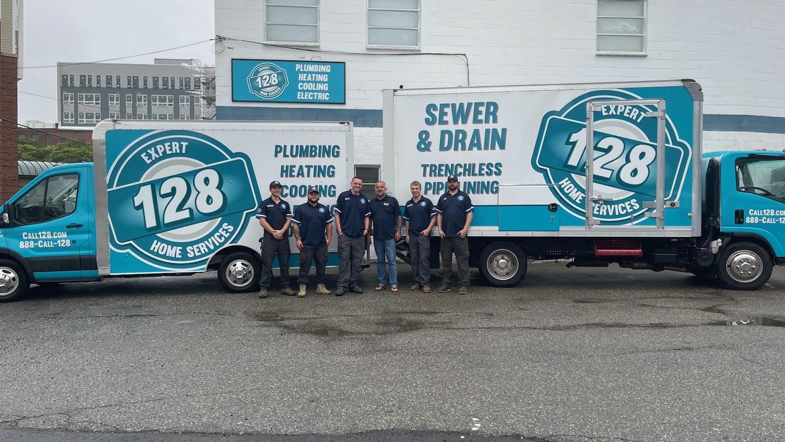 Six people in uniform stand in front of two blue and white service trucks, proudly displaying logos for Expert 128 Home Services, your dependable Boston emergency plumber offering plumbing, heating, cooling, and sewer & drain services.