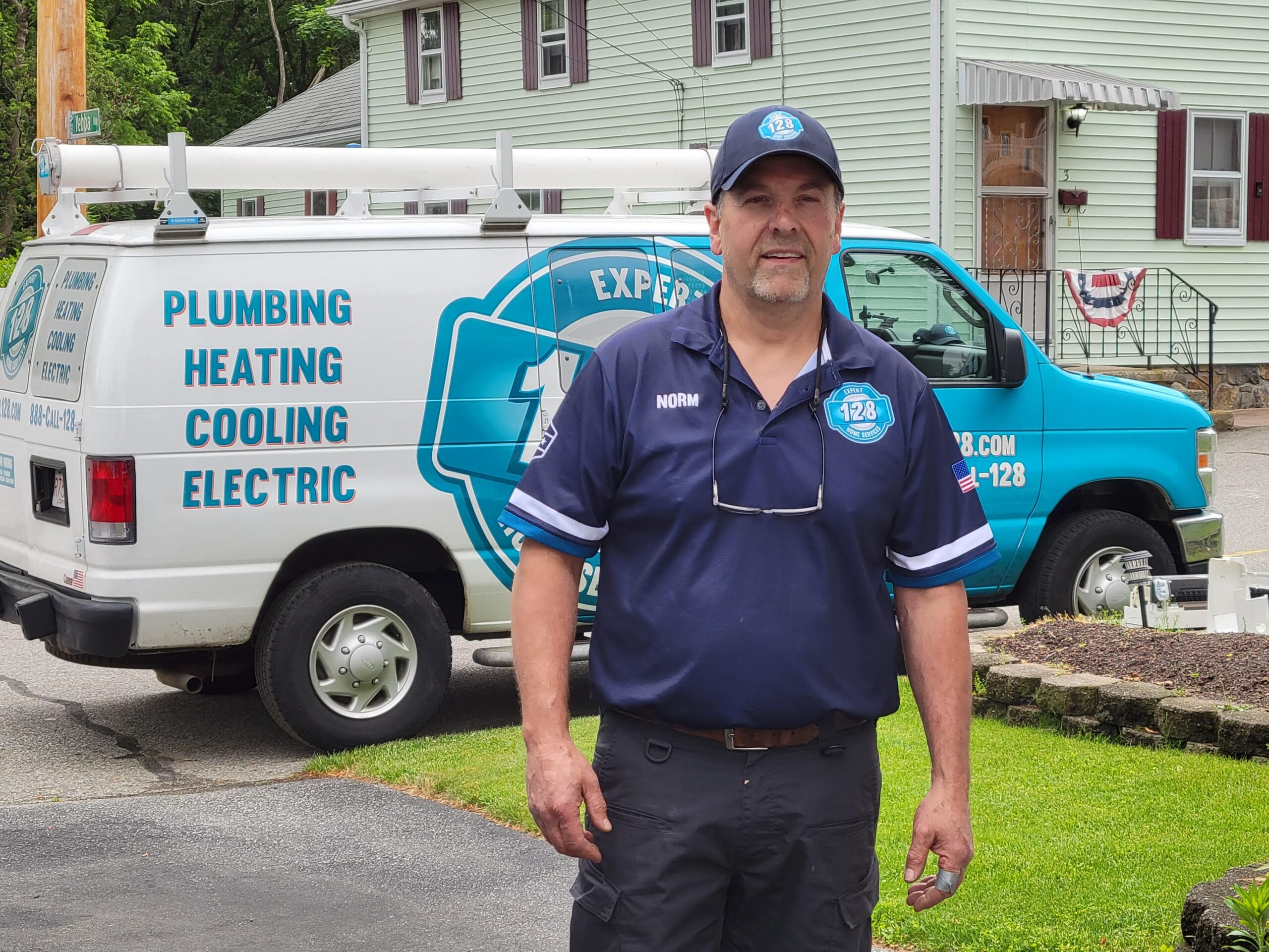 Man in uniform stands in front of a plumbing and heating service van in a residential area.