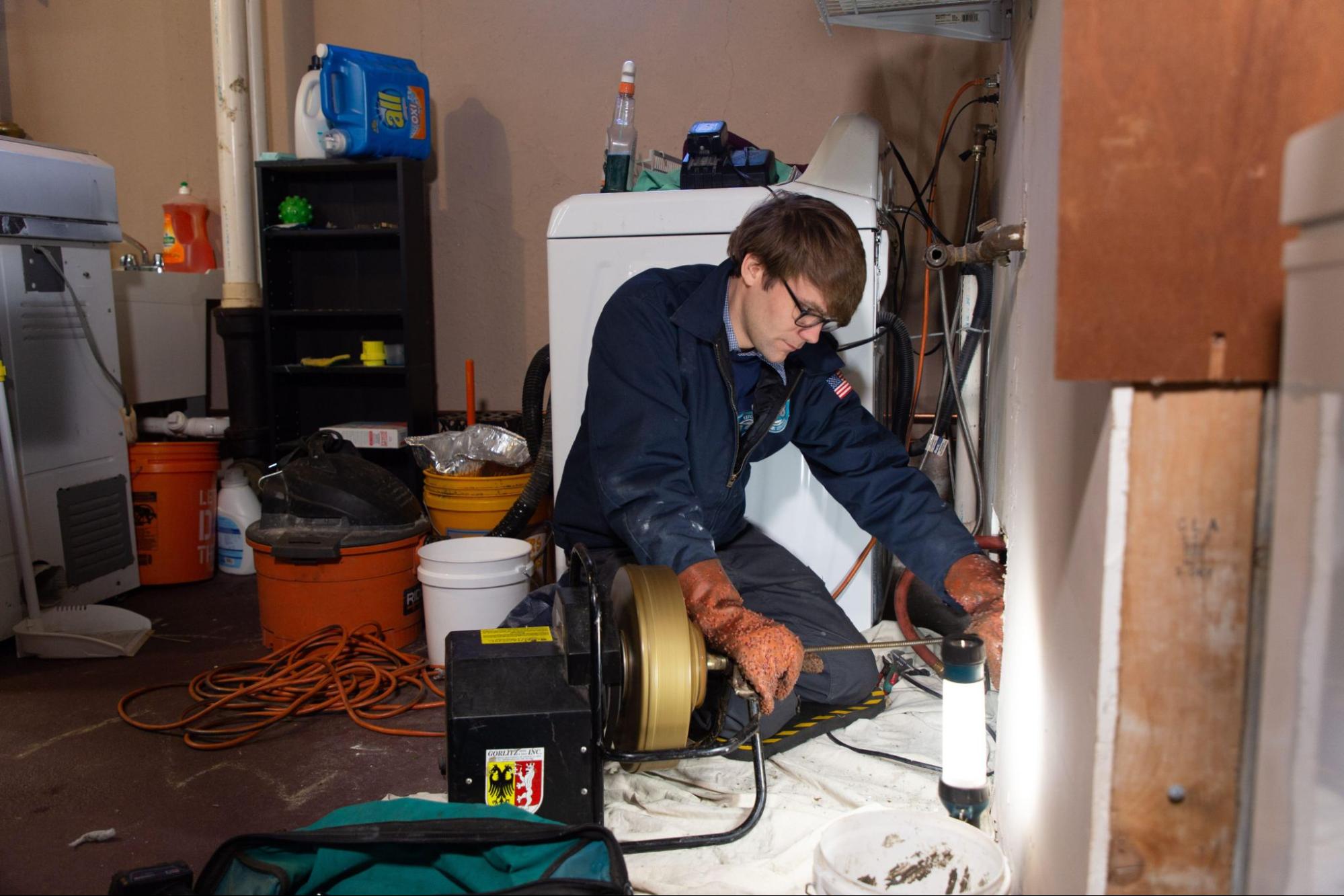 Plumber in newton ma doing drain work in 128 plumbing suit with various house items around