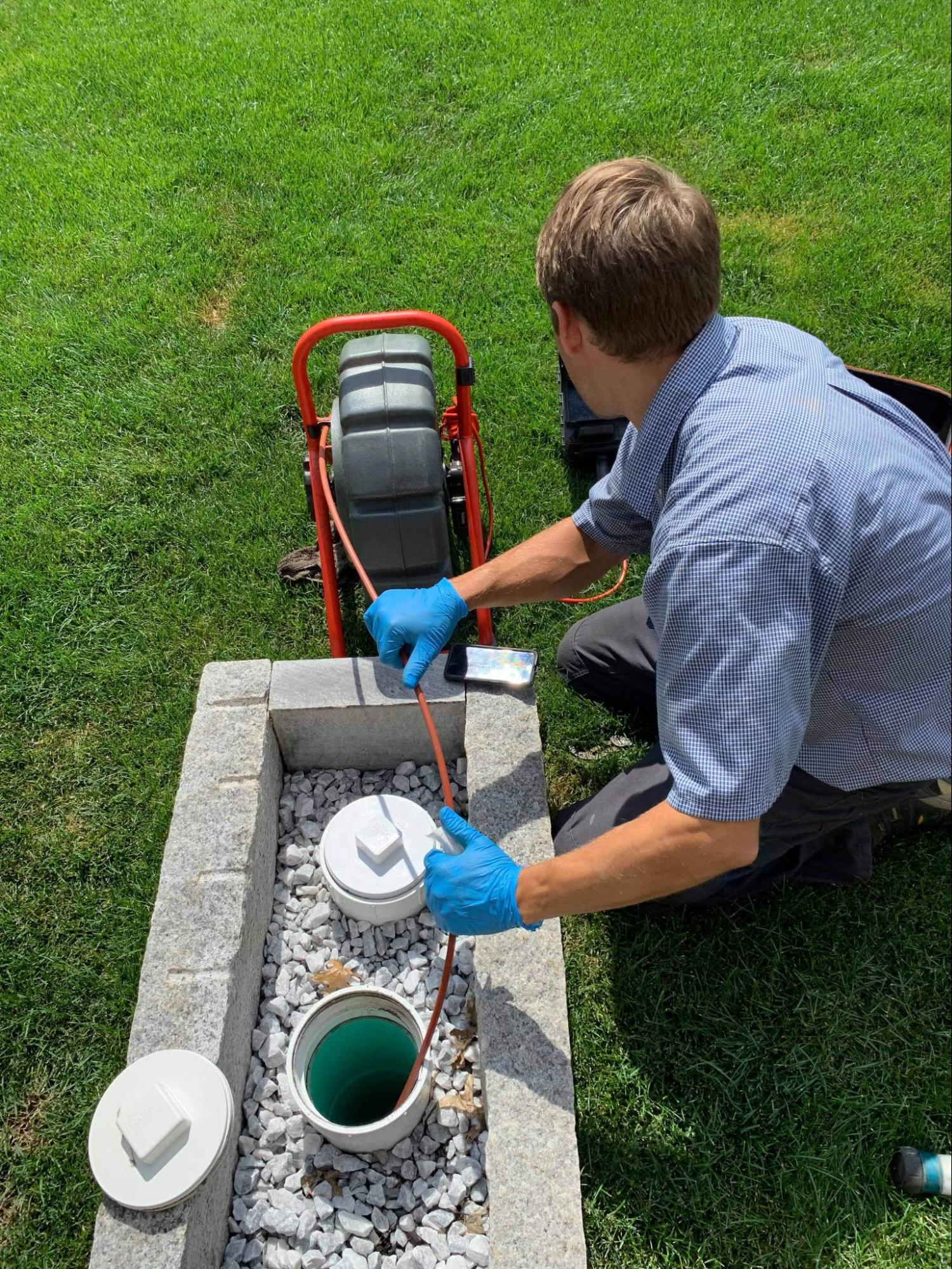 A 128 plumbing professional in blue gloves doing a drain cleaning service in Winchester, MA.
