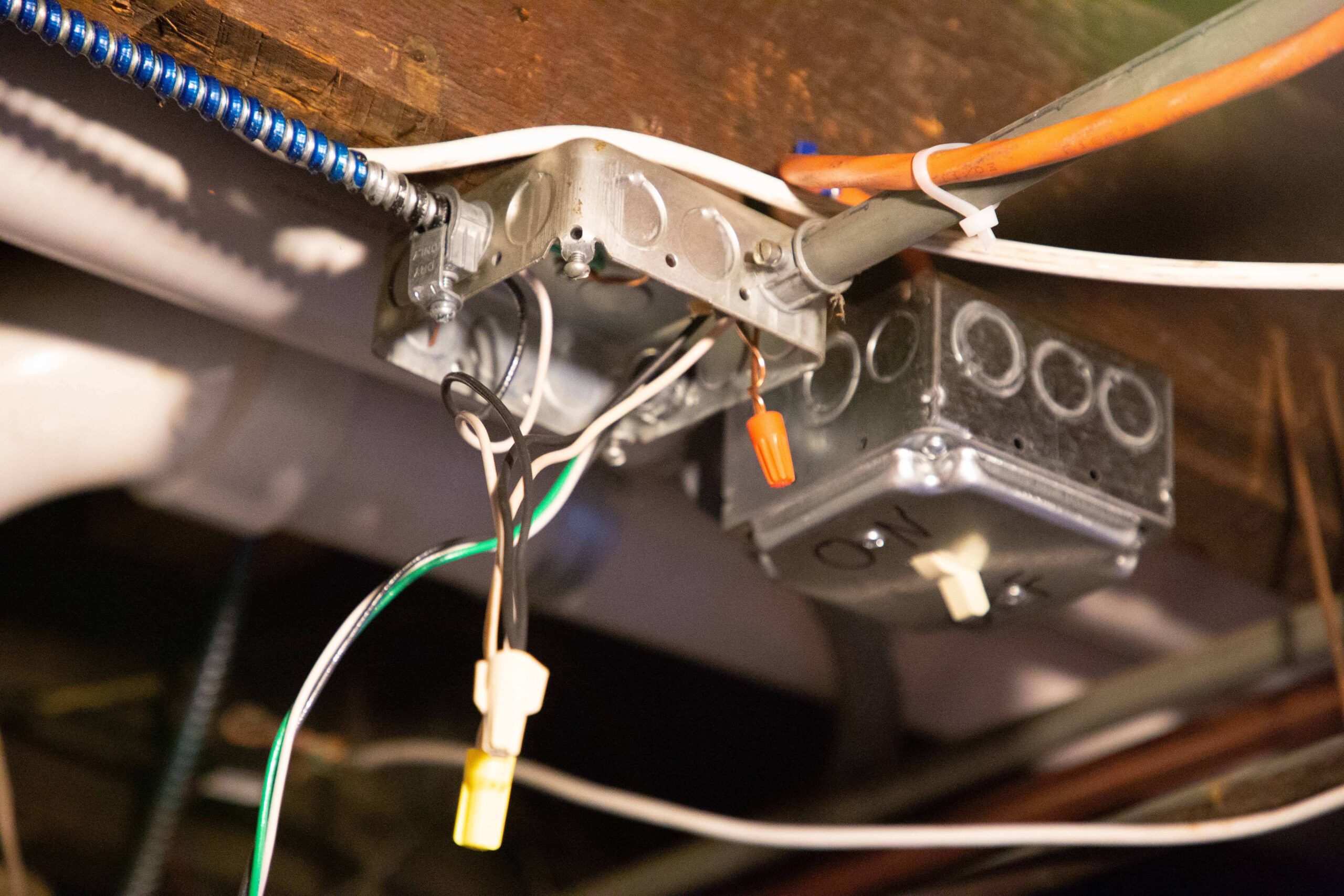 Two electrical junction boxes with exposed wires are attached to a wooden beam, awaiting the skilled touch of an electrician in South Boston, MA. Some wires are capped with connectors, while conduit lines run from the boxes, ready for professional expertise.