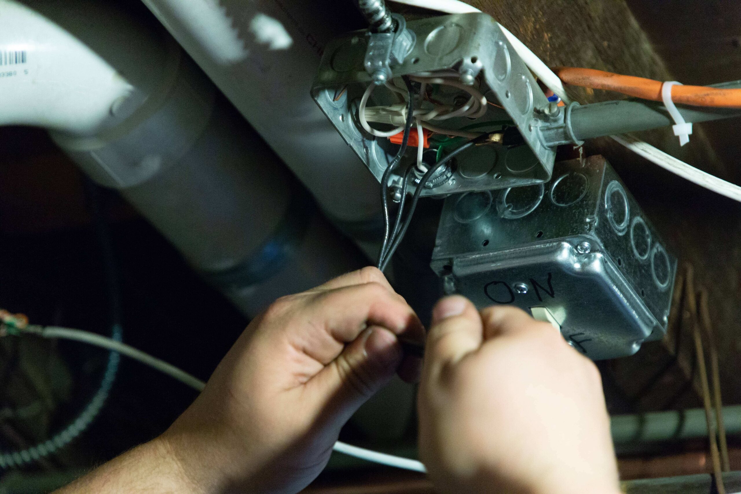 An electrician from Somerville is expertly working on electrical wiring inside a metal junction box, skillfully managing various cables in the dimly lit area.