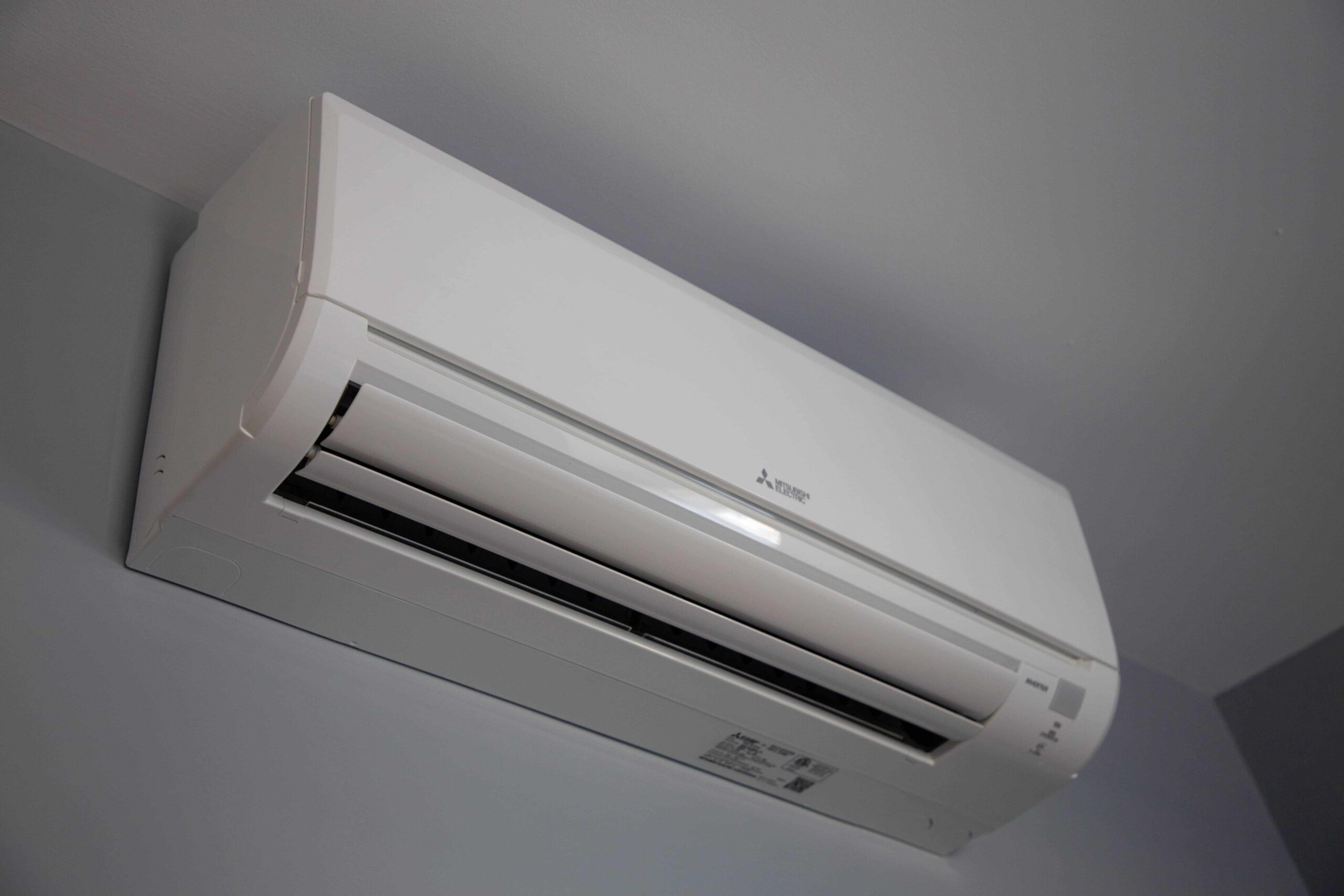 A white wall-mounted air conditioning unit, part of a ductless mini split installation, is installed inside a room with vents and control buttons visible.