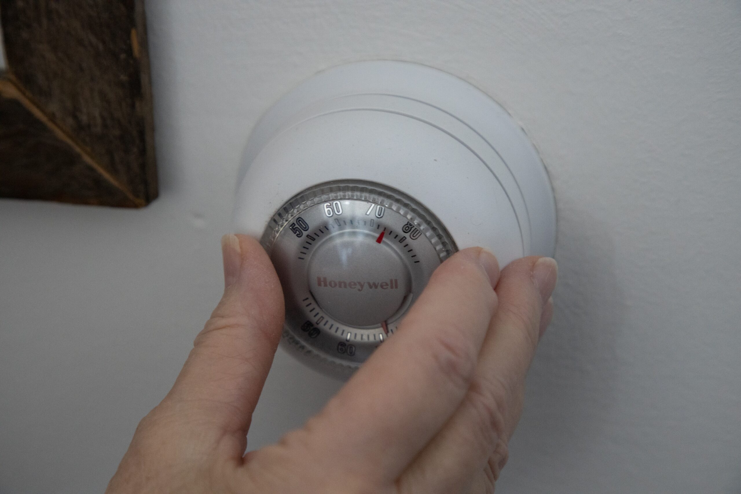 A hand adjusts the temperature on a round Honeywell thermostat mounted on a white wall, reflecting choices like oil vs gas vs electric heat for home comfort.