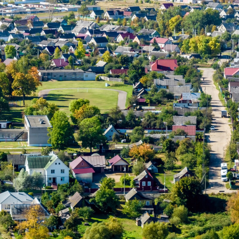 Aerial view of a small town with houses, trees, roads, and green spaces on a sunny day.
