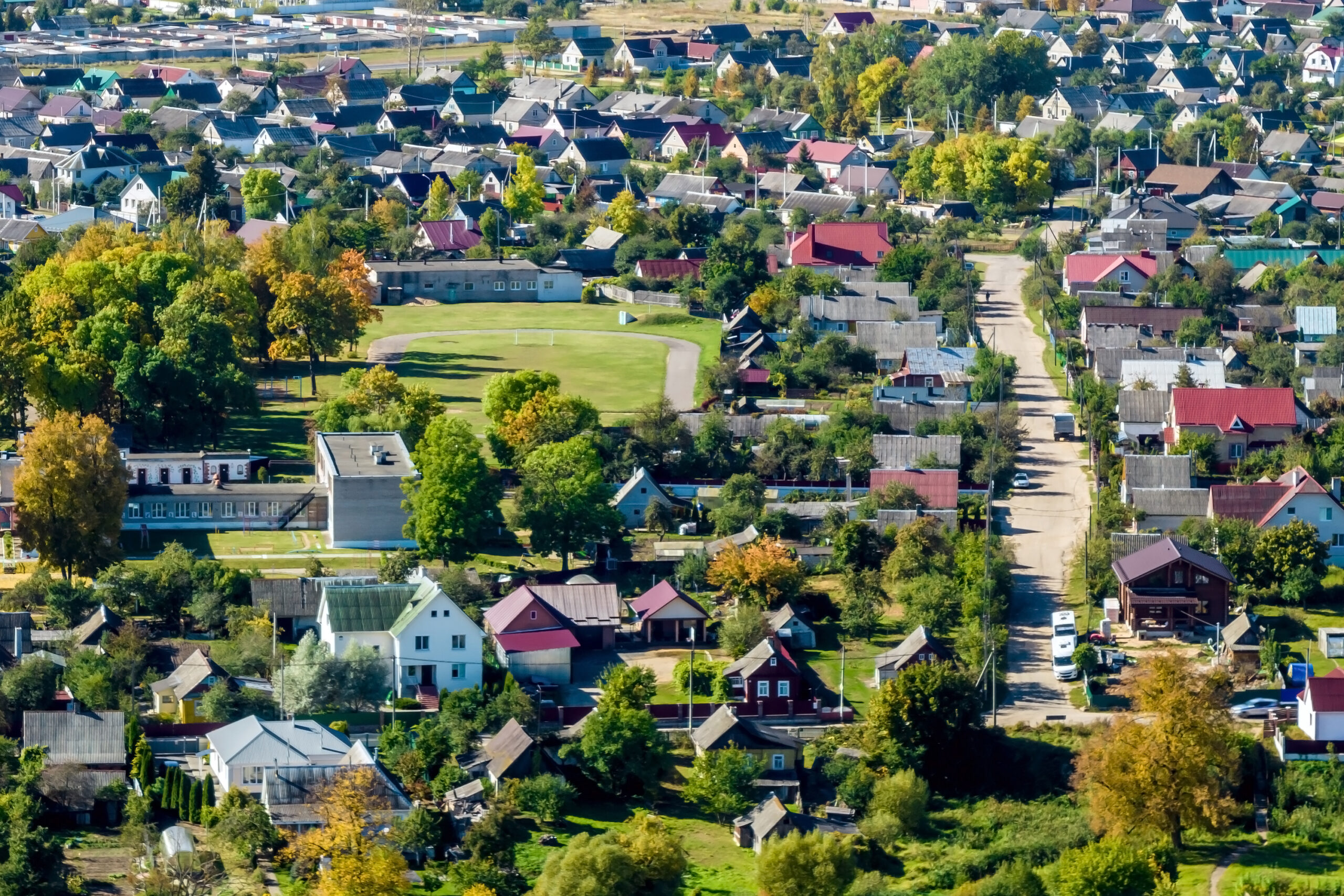 Aerial view of a small town with houses, trees, roads, and green spaces on a sunny day.